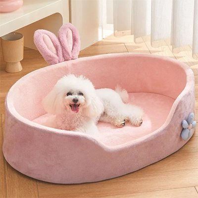 Coussin-pour-chien-chiot-lavable-déhoussable avec coussin amovible épais en coton haute densité et antidérapant-un petit chien couché confortablement dans son panier avec haut rebords anti-stress et entourant de couleur rose avec oreille de lapin et fleur en décoration dans le salon de l'appartement