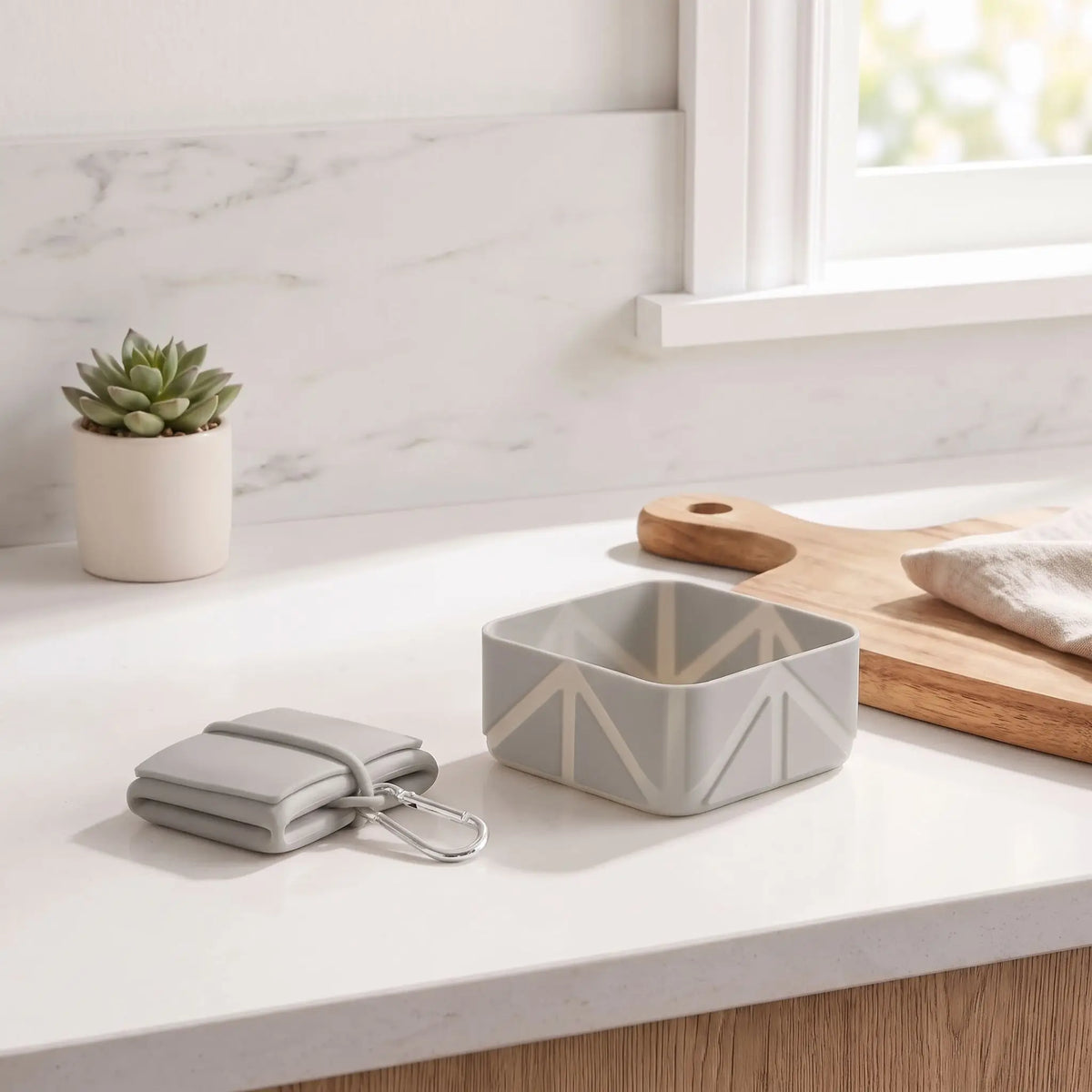 Gamelle-pliable-pour-chien-lot-de-2-avec-mousqueton en silicone alimentaire, ultra-compacte, ultra-légère, antidérapante, lavable, robuste d'une contenance de 500 ml par gamelle, soit 1 litres avec le lot de deux gamelles pour chiot et chien de petite à moyenne taille-gros plan sur le lot des 2 gamelles pliable et compacte en silicone lavable avec son mousqueton de transport de couleur grise en version dépliée et pliée sur le meuble de la cuisine de l'appartement