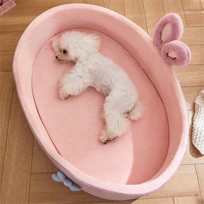 Panier-pour-chien-de-petite-taille-un caniche blanc qui dort confortablement sur le flanc dans son panier avec coussin épais haute densité 100% coton déhoussable et lavable antidérapant de couleur rose avec design lapin et fleur dans le salon de la maison