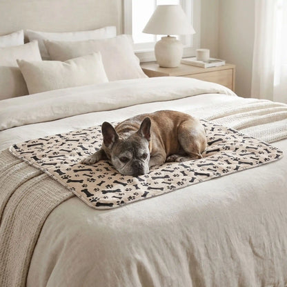 Alèse-lavable-chien-chiot-apprentissage-proprete-chien âgés, incontinent, 100% imperméable, lavable en machine, résistant aux griffes, durable, vendu en lot de deux, écoresponsable et écologique-un bouledogue français qui se repose couché sur le tapis absorbant beige marron avec imprimé os et pattes de chiens de couleur noir sur le lit de son maitre 