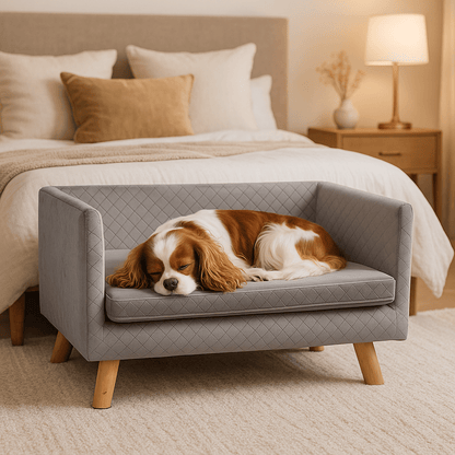 Canapé-chien-avec-coussin amovible épais et rembourré de mousse 100% coton haute densité déhoussable et lavable en machine-structure en bois avec pieds en bois de bouleau massif solide et robuste-anti affaissement-au design scandinave et moderne pour chien de petite taille jusqu'à 7 kg max-un Cavalier King Charles qui dort paisiblement couché sur son canapé gris surélevé sur pied dans la chambre moderne de l'appartement