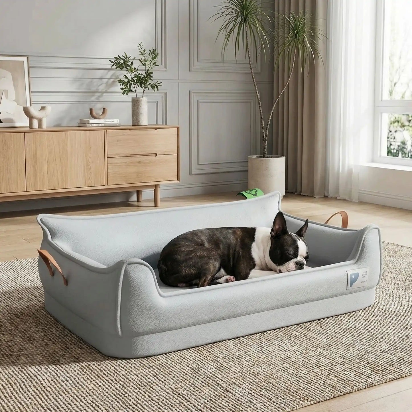 Canape-orthopedique-chien-chiot-imperméable, déhoussable, antidérapant et lavable avec deux poignée de transport semblable à un panier avec dossier et rebord en accoudoir, résistant aux griffes en cuir végan et matelas haute résilience à mémoire de forme en coton PP, design moderne et soigné avec coutures solides pour chiot et chien de petite à moyenne taille-un Boston Terrier qui dort paisiblement niché dans son canapé en forme de panier design et moderne de couleur gris dans le salon de l'appartement