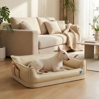 Canape-orthopedique-chien-chiot-imperméable, déhoussable, antidérapant et lavable avec deux poignée de transport semblable à un panier avec dossier et rebord en accoudoir, résistant aux griffes en cuir végan et matelas haute résilience à mémoire de forme en coton PP, design moderne et soigné avec coutures solides pour chiot et chien de petite à moyenne taille-un Bull terrier couché confortablement dans son canapé en forme de panier design et moderne de couleur beige dans le salon de la maison
