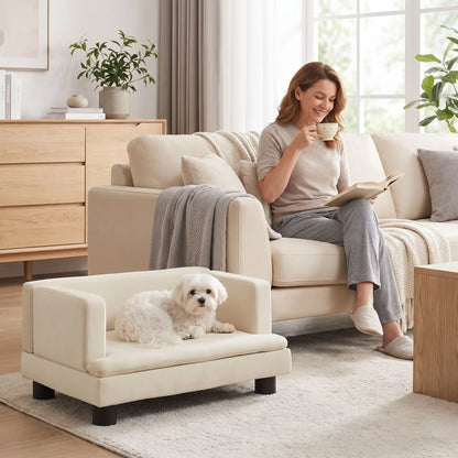 Canapé-pour-petit-chien-chiot-surélevé de 80 cm, structure en bois massif avec 4 pieds en bois et housse en velours doux et résistant aux griffes avec dossier haut en U entourant et enveloppant de forme rectangulaire, avec matelas épais en éponge coton haute densité et haute résilience pour un couchage ergonomique pour chien de petite à moyenne race, robuste avec une capacité de charge de 30 kilos-un chien de petite race couché confortablement dans le canapé en velours blanc crème sur 4 pieds dans le salon