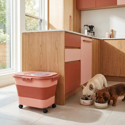 Conteneur-a-croquettes-pour-chien-sur 4 roulettes amovibles, pliable avec fenêtre hermetique de contrôle de niveau- contenance de 10 à 12 kg de croquettes-lavable, résistant, compactable en accordéon, transportable pour protéger la fraicheur et protéger la nourriture des insectes ou nuisible-photo du conteneur rose dans la cuisine avec deux chiens qui mangent dans leur gamelle à côté