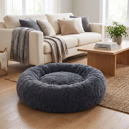 Coussin-déhoussable-pour-chien-chiot-antistress en peluche douce et hypoallergénique, lavable en machine, fond antidérapant et imperméable, en forme de beignet rond avec rebord surélevé 360°, rembourrage 100% coton haute densité, disponible en 5 tailles du S au XXL en 3 coloris rose, gris et gris foncé pour chien de 0 à 40 kg max-gros plan sur le coussin entourant et douillet de couleur  gris foncé  de taille XXL sur le sol du salon de l'appartement