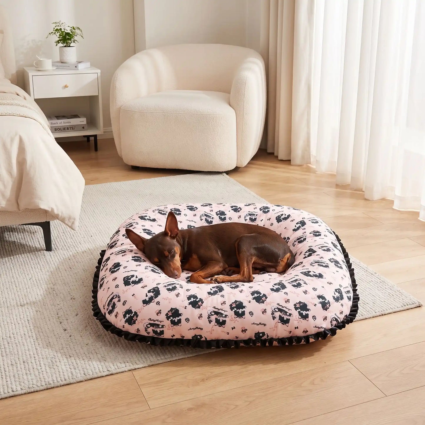 Coussin-petit-chien-chiot-cosy-avec rebord 360° entourant surélevé pour envelopper et avoir un effet anti-anxiété, rembourrage 100% coton haute densité, tissu 100% imperméable, lavable en machine, de forme carré pour une utilisation polyvalente ou donner plus de confort au couchage, en 3 tailles XS, S et M pour chiots et chiens de 0 à 9 kg-un chien de race naine qui dort en boule niché dans le coussin épais ergonomique au rebord large et entourant au pied du lit de ses maitres dans la chambre