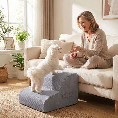 Escalier pour chien-chiot-en mousse, antidérapant, déhoussable lavable en machine avec mousse haute résilience à mémoire de forme pour protèger les articulations sensibles, sécurisé , confortable, résistant aux griffes pour petit et chien de moyenne taille, disponible en 2 modèles 2 marches et 3 marches-un chien de petite taille qui monte confortablement sur l'escalier de 2 marches en mousse gris clair pour rejoindre sa maitresse qui l'appelle, assise pour des calins sur le canapé du salon de la maison