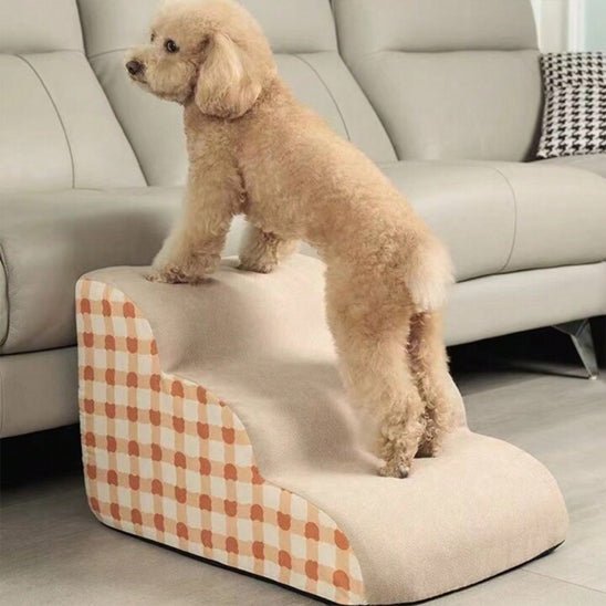 Escalier-mousse-pour_chien-chiot-antidérapant, déhoussable lavable en machine avec mousse haute résilience à mémoire de forme pour protèger les articulations sensibles, sécurisé , confortable, résistant aux griffes pour petit et chien de moyenne taille-design velours sur le dessus ultra-doux et tissu en coton solide avec motif orange à carreaux style vichy-un petit chien qui monte confortablement sur l'escalier de 3 marches en mousse pour monter sur le canapé du salon en toute sécurité