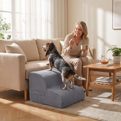 Escalier pour chien-chiot-en mousse, antidérapant, déhoussable lavable en machine avec mousse haute résilience à mémoire de forme pour protèger les articulations sensibles, sécurisé , confortable, résistant aux griffes pour petit et chien de moyenne taille, disponible en 2 modèles 2 marches et 3 marches-un chien de race à pattes courtes qui monte confortablement sur l'escalier de 2 marches en mousse gris foncé pour rejoindre sa maitresse qui l'appelle, assise sur le canapé du salon de l'appartement