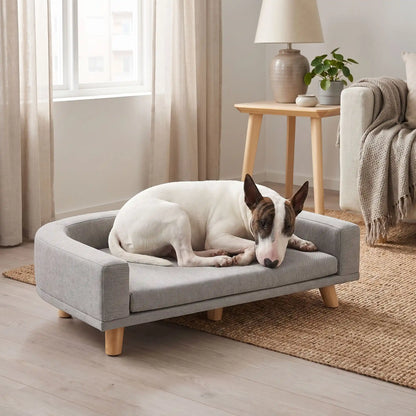 Fauteuil-pour-chien-design-bois-massif-velours, coussin amovible déhoussable et lavable, matelas orthopédique à mémoire de forme en éponge coton haute densité d'épaisseur de 4 cm, structure robuste en bois massif au design moderne et lignes arrondies et épurées avec dossier et acoudoirs enveloppants de couleur gris et pieds en bois naturel, style scandinave pour chiot et chien de petite à moyenne taille- un chien moyen qui dort paisiblement sur le flanc niché dans le fauteuil surélevé gris sur pieds  