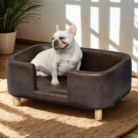 Fauteuil-pour-petit-chien-imperméable-hygiénique-avec matelas amovible épais avec pied en bois de bouleau massif design soigné forme arrondie et lignes épuré en simili cuir chocolat-un chien de petite taille heureux dans son mini canapé de forme rectangulaire comme un panier entourant surélevé dans le salon de l'appartement