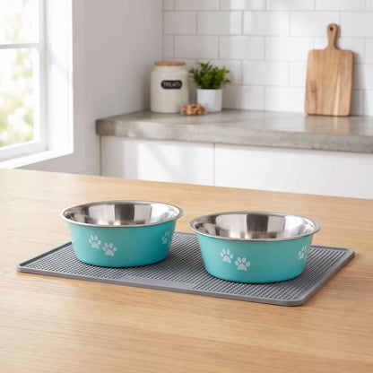 Gamelle-chien-chiot-lot-de-2-inox durable et robuste, design bleu ou gris avec pattes de chiens blanches , lavable en lave -vaisselle avec fond 360° en caoutchouc antidérapant et anti renversement, anti-rayures au sol, disponible en 4 tailles : 400/800 ml ou 1,5/2 litres pour chiot et chien de petite, moyenne et grande race- gros plan sur les deux gamelles en inox hygiénique teinté à l'exterieur d'un design bleu cieavec pattes de chien blanches sur le tapis pour gamelle gris sur le meuble de la cuisine 