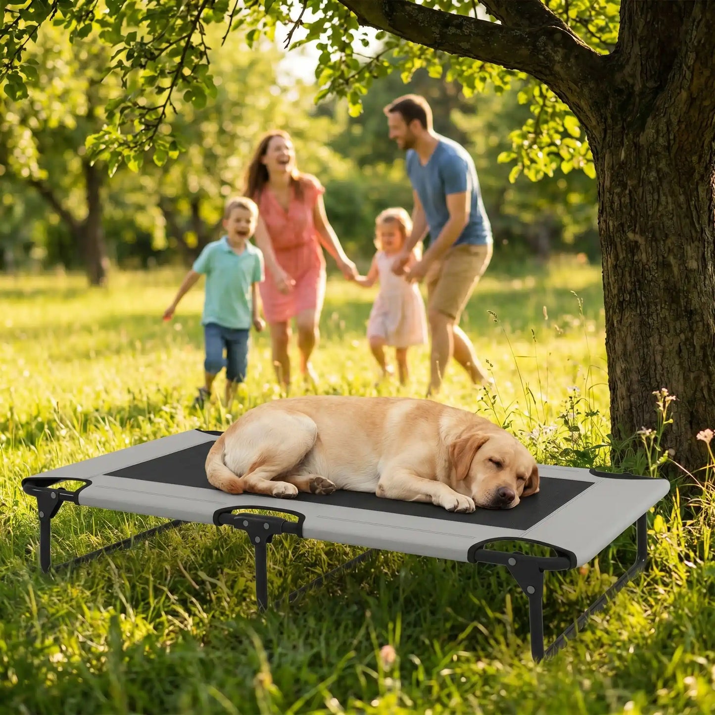 Hamac pour chien de 107 cm, en tissu oxford 100% imperméable et maille respirante et structure en acier robuste, polyvalent pour une utilisation interieur et exterieur, surélevé avec 3 barres transversales et patin anti rayure pour une stabilité pour chiot et chien de petite à moyenne taille jusqu'à 30 kilos-un chiende race moyenne qui dort couché au frais sur son lit surélevé dans le jardin à côté de sa famille qui jouent en vacances en été