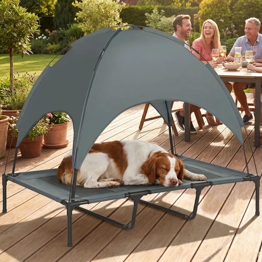 Lit-camp-chien-auvent-120-cm, en tissu oxford 100% imperméable et maille respirante et structure en acier inoxydable, avec son dôme parasol amovible anti uv et anti pluie, polyvalent pour une utilisation interieur et exterieur, surélevé avec 4 pieds et deux barres transversales au milieu et patin anti rayure pour une stabilité pour chiot et chien de petite à moyenne taille jusqu'à 30 kilos-un chien moyen couché au frais sur son lit de camp avec auvent sur la terasse avec ses maitres qui boivent l'apéro 
