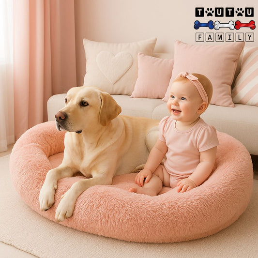 Lit-chien-xxl-déhoussable-un labradorcouché avec un bébé assis à côté de lui dans le grand lit ovale avec rebord haut entourant à 360° spacieux en peluche douce rose avec matelas orthopédique à mémoire de forme 100% coton haute densité lavableen machine dans le salon cosy de la maison