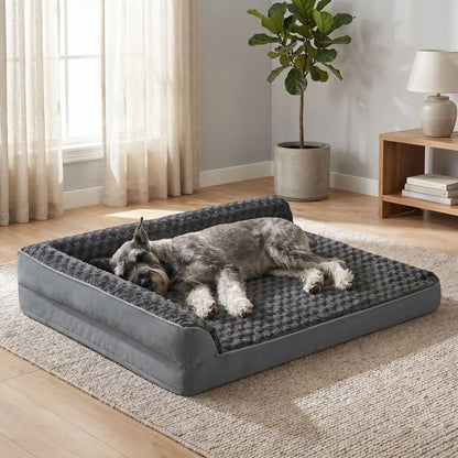 Lit-grand-chien-chiot-orthopédique-xxl avec traversin intégré,antidérapant-imperméable-déhoussable-lavable en machine-résistant aux griffes et morsures  pour grand chien et chiot jusqu'à 50 kg max-en velours côtelé et 100% Coton PP et deux traversins cylindriques rembourré en forme de L de couleur gris pour un effet apaisant et sécurisant-un Schnauzer couché confortablement sur le flanc sur son lit orthopédique en forme de canapé gris avec ses deux traversins surélevés  dans le salon de l'appartement