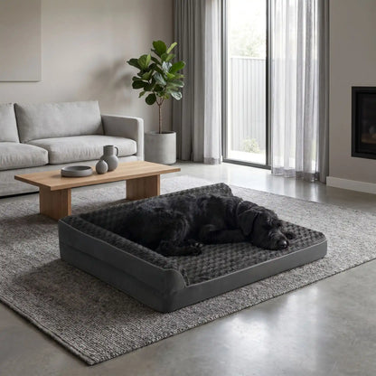 Lit-grand-chien-chiot-orthopédique-xxl avec traversin intégré,antidérapant-imperméable-déhoussable-lavable en machine-résistant aux griffes et morsures  pour grand chien et chiot jusqu'à 50 kg max-en velours côtelé et 100% Coton PP et deux traversins cylindriques rembourré en forme de L de couleur gris pour un effet apaisant et sécurisant-un  chien de grande race qui dort paisiblement niché dans l'angle du lit orthopédique , sa tête reposant sur la housse en velours et peluche  du lit à mémoire de forme 