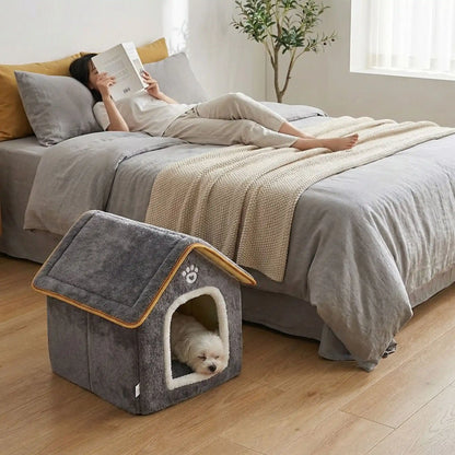 Maison-chien-intérieure-chiot-mini, pliable, légère et transportable, avec matériau isolant efficace contre le bruit et du froid, niche antidérapante, lavable en machine avec toit amovible, de couleur grise pour chiot et chien de 0 à 5 kg, disponible en taille XS et S- un chien de petite taille qui dort paisiblement dans la petite niche intérieure sur le sol de la chambre à côté du lit de sa maitresse allongé qui lit son livre tranquillement
