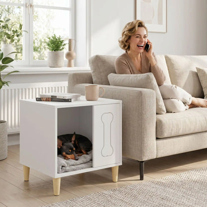 Meuble-niche-chien-interieur en bois et au design contemporain de forme cubique sur 4 pieds surélevés en bois antidérapant avec un décor d'os gravé sur l'avant avec ouverture pour une entrée et descente facile sur un quart du meuble pour chiot et chien de petite taille de 0 à 3 kg-un Pinscher nain qui dort paisiblement dans sa niche en bois design qui sert de meuble d'appoint à côté du canapé où sa maitresse est assise au téléphone dans le salon de l'appartement