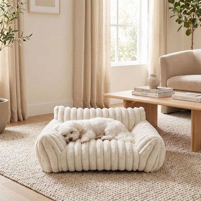 Mini-canapé-chien-chiot-déhoussable, lavable en machine ,coton, housse en peluche douce au toucher velours, rembourrage ergonomique en mousse à mémoire de forme pour un soutien optimal, disponible en  couleurs blanc et rose et 3 tailles S, M et L pour chiot et chien de petite taille de 0 à 10 iols max-un chien de petite taille qui dort paisiblement niché contre le dossier haut et l'accoudoir rembourré du mini fauteuil pour chien de couleur blanc crème dans le salon de la maison