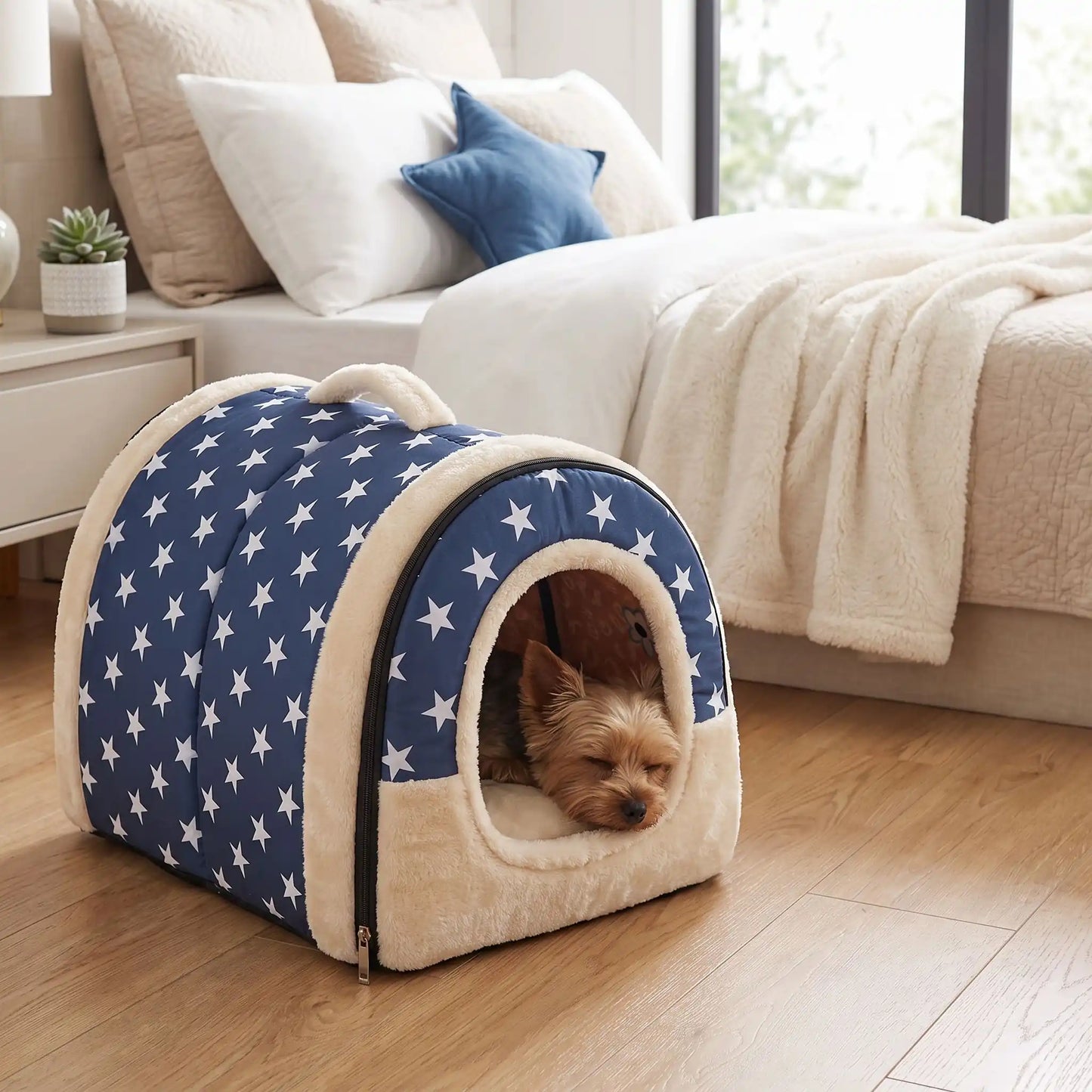 Niche chien et chiot intérieur de petite race, résistante, en forme d'igloo au design sécurisant fermée en arc de cercle avec un coussin rectangulaire au rembourrage 100% coton haute densité lavable,double face été en tissu/hiver en peluche  et fond antidérapant et extérieur 100% imperméable, transportable avec sa poignée, lavable- un petit chien couché confortablement au chaud dans sa niche douillette, chaude sécurisante à 360° avec design américain bleu et étoiles blanches au pied du lit de sa maitresse 