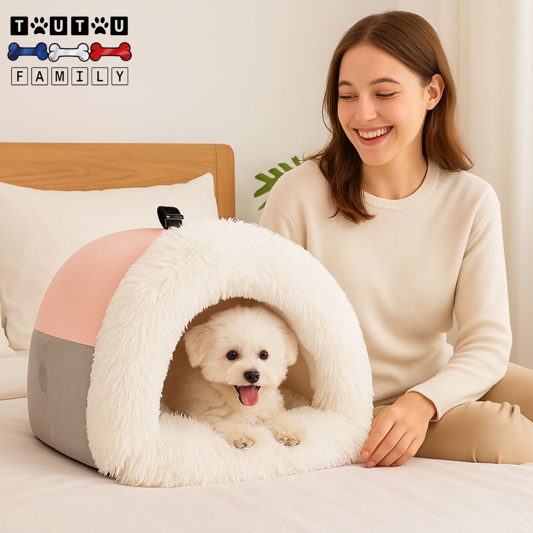 Niche-pour-chien-interieur-portable-chaude- une femme souriante assise sur le lit avec son petit chien couché dans sa niche rose et grise avec poignée posé à côté d'elle sur le lit
