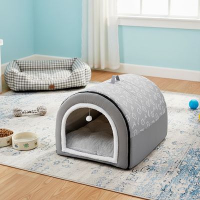 Niche-pour-chiot-anti-stress, en forme de grotte ou d'igloo semi-fermé pour une bonne isolation sonore qui protège du froid, un refuge sécurisé avec ubn coussin intérieur amovible et lavable en machine, structure robuste et pliable 100% imperméable et résistant, antidérapant, transportable avec sa poignée intégrée pour chiot de 0 à 15 kilos-photo de la niche pour chiot de couleur grise avec sa balle suspendue sur sa corde interactive à la porte d'entrée 
