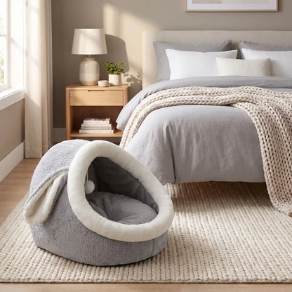 Panier-chien-chiot-niche-anti-stress, conception semie fermée avec toit et coussin amovible en velours rembourrage 100% coton PP, niche en peluche douce et design mignon avec oreilles de lapin, fond antidérapant et imperméable, lavable en machine pour chiot et chien de petite race de 0 à 3 kg-gros plan sur le panier avec toit en dôme comme une cabane en peluche douce et oreilles de lapin de couleur gris et blanc au pied du lit de ses maitres dans la chambre de la maison