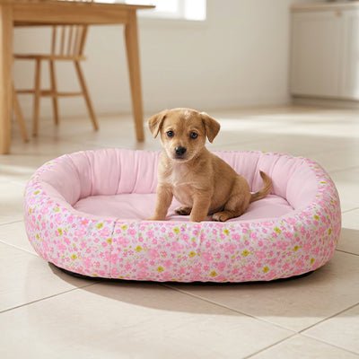 Panier-chien-coussin-4-saisons, 100% coton haute densité, ergonomique et rembourré, avec rebord surélevé épais à 360° pour un effet anti stress, entourant et enveloppant-coussin intérieur moelleux qui soutient et protège les articulations, lavable en machine et antidérapant-couchage pour chiot et chien de petite à moyenne taille de 0 à 15 kilos max-un chiot confortablement assis dans le panier ovale de couleur rose dans la cuisine de la maison