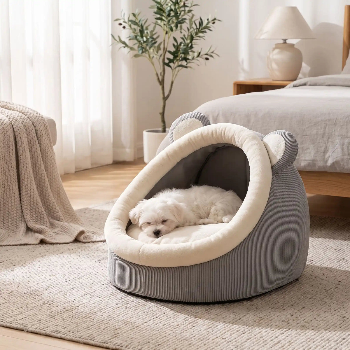 Panier-chien-chiot-niche-anti-stress, conception semie fermée avec toit et coussin amovible en velours rembourrage 100% coton PP, niche en peluche douce et design mignon avec oreilles d'ours, fond antidérapant et imperméable, lavable en machine pour chiot et chien de petite race de 0 à 3 kg-un chiot de petite race qui dort couché confortablement dans son panier avec toit en dôme comme une cabane en peluche douce et oreilles d'ours de couleur gris et blanc au pied du lit dans la chambre de l'appartement