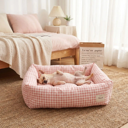 Panier chien et chiot rectangulaire avec rebord 360° surélevé en tissu pour chien de petite taille, 100% coton haute densité avec coussin intérieur amovible double-face été/hiver lavable en machine avec fond imperméable et antidérapant, design à carreaux vichy chic et frais pour un lit 4 saisons pour chien et chiot de 0 à 9 kilos-un chien de race naine qui dort paisiblement les pattes à l'air dans le panier rectangulaire vichy de couleur rose au pied du lit de son maître dans la chambre de la maison