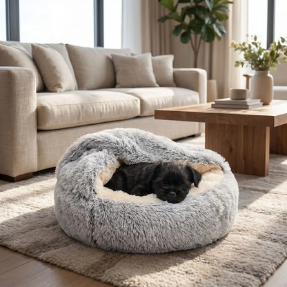 Panier-couvert-chien-chiot douillet, lit en peluche rond avec toit souple qui sert de couverture cousue au panier rond et profond comme un donut au rembourrage 100% coton haute densité entourant et ergonomique pour un effet apaisant et anti-stress, chaud pour les chiots et chiens de petite taille de 0 à 5 kg, anxieux ou frileux-un chien de race naine qui dort niché dans son panier rond gris avec le toit reposant sur son corps pour un effet calmant qui protège du froid sur le sol du salon de la maison