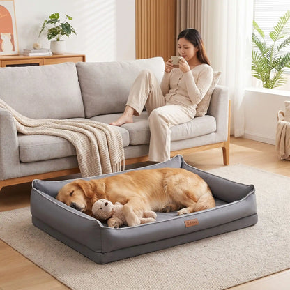 Panier-lavable-pour-chien-impermeable-4-saisons pour chiot, chien de petite, moyenne et grande taille du S au XL, avec matelas orthopédique à mémpoire de forme, déhoussable et lavable en machine, housse 100% imperméable en tissu solide et résistant, panier rectagulaire avec rebord surélevé et dossier plus haut pour un effet canapé lit pour chien-un golden retriever qui dort paisiblement,sur le flan avec sa peluche  dans le panier orthopédique au pied de sa maîtresse qui boit son café sur le canapé du salon 