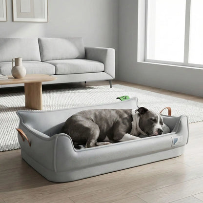 Panier-orthopedique-chien-simili-cuir-imperméable, déhoussable, antidérapant et lavable avec deux poignée de transport, ne retient pas les poils, avec dossier et rebord surélevé, résistant aux griffes en cuir végan et matelas haute résilience à mémoire de forme en coton PP, design moderne et soigné avec coutures solides pour chiot et chien de petite à moyenne taille-un Staffie qui dort paisiblement dans son panier design et moderne de couleur gris dans le salon de la maison