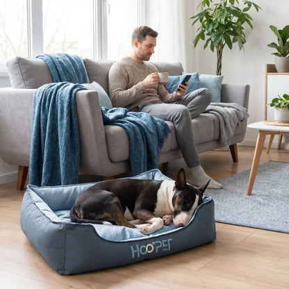Panier-tissu-chien-chiot-solide-coussin-amovible-déhoussable lavable en machine, coussin intérieur double-face : rafraichissant en été et respirant et imperméable en hiver , rembourrage généreux 100% coton haute densité et haute résilience , rectangulaire et ergonomique et confortable, antidérapant pour chiot et chien de 0 à 15 kilos-un chien de taille moyenne qui dort couché confortablement niché dans son panier gris et bleu moelleux et douillet au rembourrage coton haute densité au pied de son maitre 