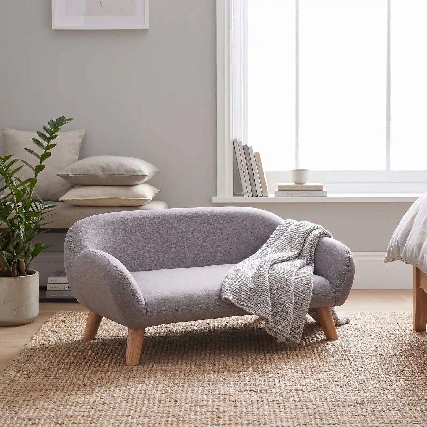 Petit-canape-pour-chien-chiot-design de couleur gris, dossier et accoudoirs arrondis dans un style scandinave, tissu résistant aux griffes, rembourrage 100% coton haute densité pour un confort optimal, structure en bois massif et surélevé avec 4 pieds en bois massif pour chiot et chien de 0 à 8 kilos-gros plan sur le petit canapé gris design compact sur pied en bois massif et rembourrage en éponge coton ergonomique pour petit chien dans la chambre de la maison