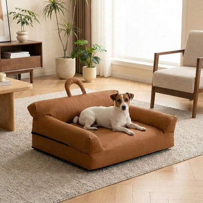Petit-canapé-pour-chien-chiot-imperméable, déhoussable lavable en machine, en Cuir végan et rembourrage 100% coton haute densité et résilience, avec accoudoirs, dossier et assise ergonomique, avec poignée de transport, antidérapant et anti humidité, durable solide et résistant aux griffes pour chiot, petit chien et race naine de 0 à 10 kilos- un petit chien blanc et marron à poils courts couché confortablement sur son mini canapé marron dans le salon de l'appartement