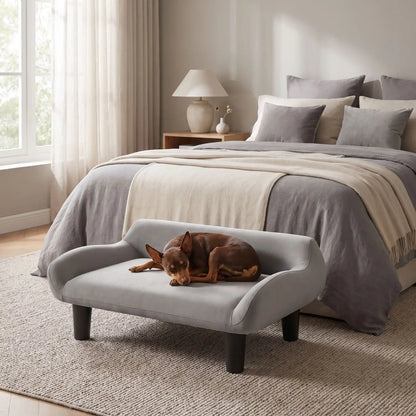 Petit-fauteuil-pour-chien-chiot-design de couleur gris, dossier et accoudoirs arrondis dans un style scandinave, velours résistant aux griffes,rembourrage 100% coton haute densité pour un confort optimal,structure en bois massif et surélevé avec 4 pieds en bois massif pour chiot et chien de 0 à 8 kilos-un chien de race naine qui dort confortablement sur son canapé gris design sur pied en bois massif et rembourrage en éponge coton ergonomique au pied du lit de sa maitresse dans la chambre de l'appartement