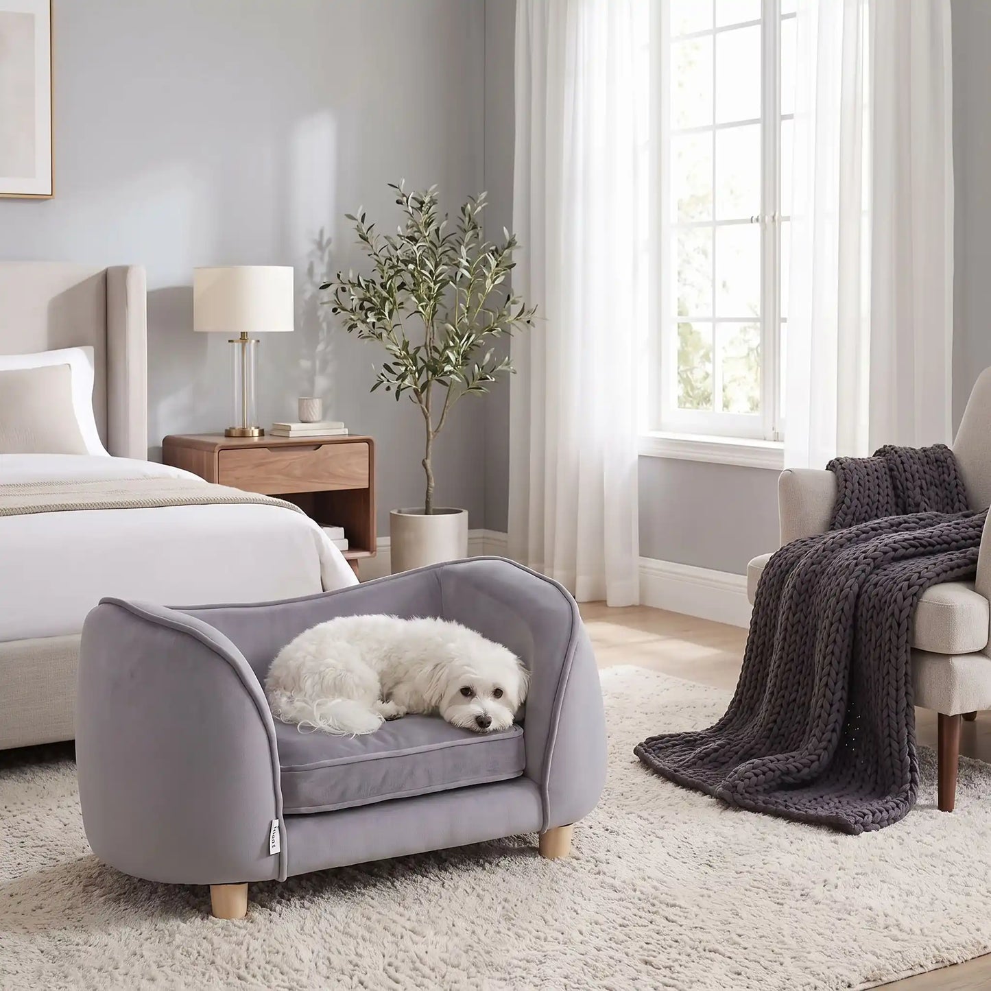 Petit-fauteuil-pour-chien-chiot-coussin intérieur épais au rembourrage 100% coton ergonomique, velours doux et résistant aux griffes, imperméable déhoussable et lavable en machine, de couleur gris, au design enveloppant en forme bateau structrure en bois massif avec 4 pieds à vissés en bois massif et robuste pour chiot et chien de petite taille à moyenne taille-un chien de petite taille qui dort paisiblement enveloppé dans son fauteuil avec son haut dossier au pieds du lit de ses maitres dans la chambre