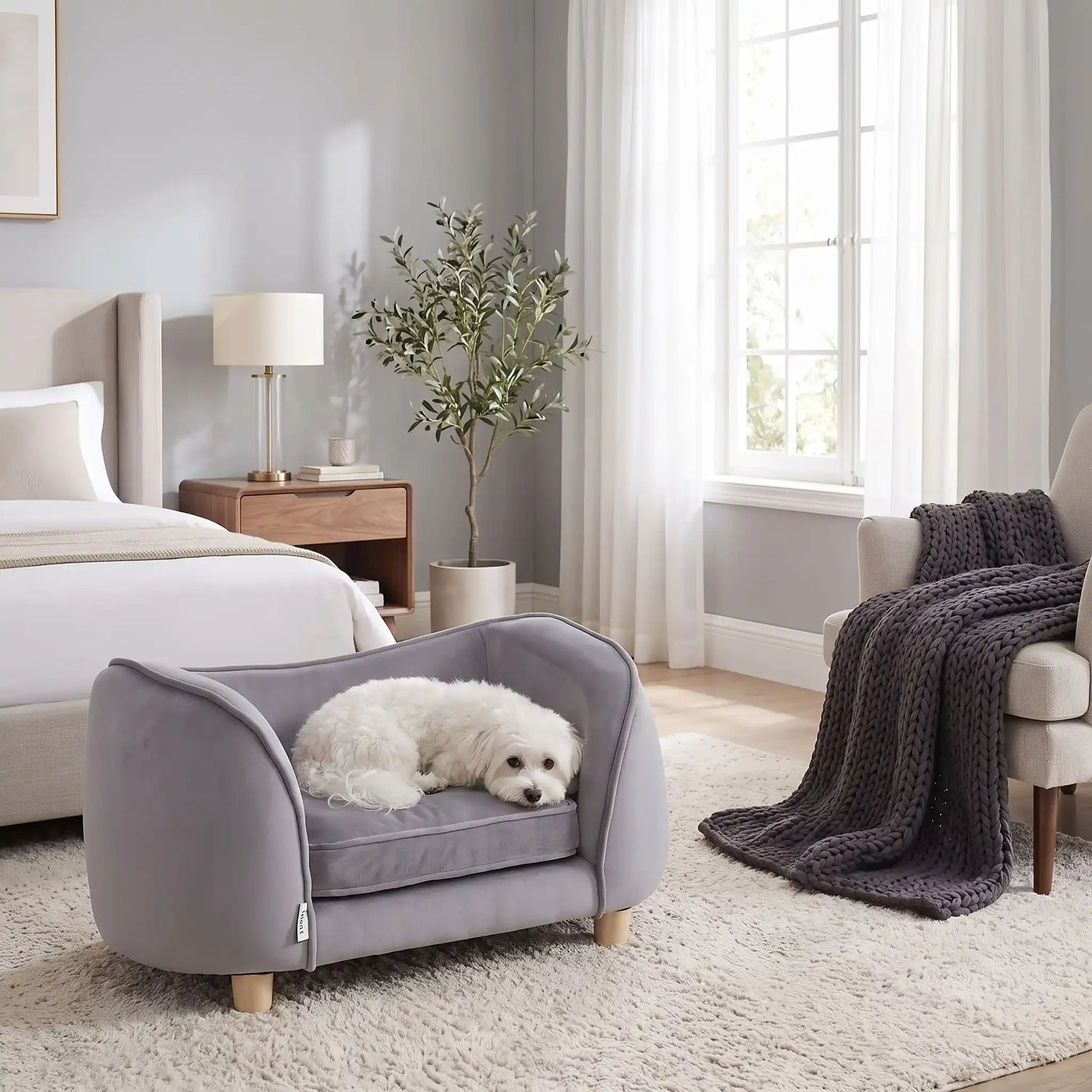 Petit-fauteuil-pour-chien-chiot-coussin intérieur épais au rembourrage 100% coton ergonomique, velours doux et résistant aux griffes, imperméable déhoussable et lavable en machine, de couleur gris, au design enveloppant en forme bateau structrure en bois massif avec 4 pieds à vissés en bois massif et robuste pour chiot et chien de petite taille à moyenne taille-un chien de petite taille qui dort paisiblement enveloppé dans son fauteuil avec son haut dossier au pieds du lit de ses maitres dans la chambre