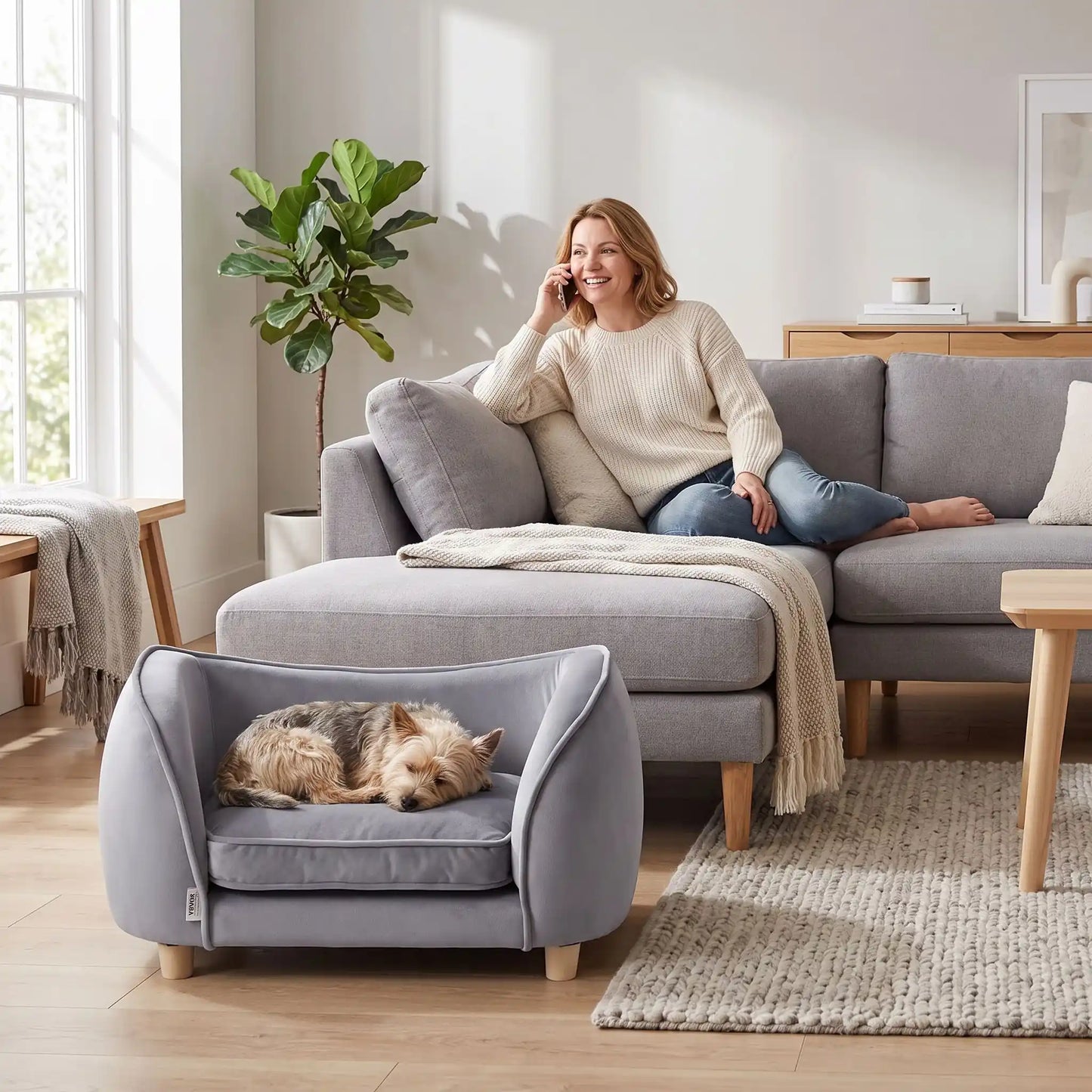 Petit-fauteuil-pour-chien-chiot-coussin intérieur épais au rembourrage 100% coton ergonomique, velours doux et résistant aux griffes, imperméable déhoussable et lavable en machine, de couleur gris, au design enveloppant en forme bateau structrure en bois massif avec 4 pieds à vissés en bois massif et robuste pour chiot et chien de petite taille à moyenne taille-un chien de petite race qui dort paisiblement enveloppé dans son fauteuil avec son haut dossier au pied du canapé de sa maitresse dans le salon