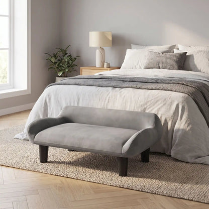 Petit-fauteuil-pour-chien-chiot-design de couleur gris, dossier et accoudoirs arrondis dans un style scandinave, velours résistant aux griffes,rembourrage 100% coton haute densité pour un confort optimal,structure en bois massif et surélevé avec 4 pieds en bois massif pour chiot et chien de 0 à 8 kilos-gros plan sur le petit canapé gris design sur pied en bois massif et rembourrage en éponge coton ergonomique au pied du lit de sa maitresse dans la chambre de l'appartement