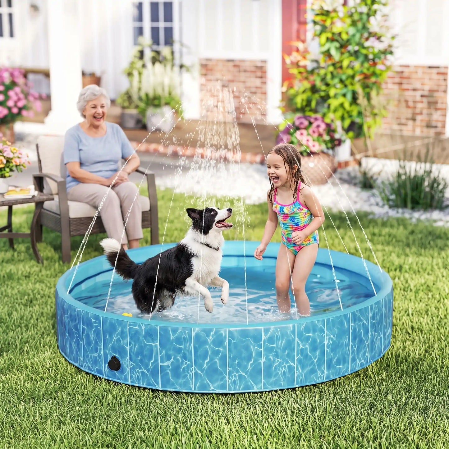 Piscine-rigide pour grand chien-xxl avec raccord universel au tuyau d'arrosage pour jets d'eau,rigide-vidange rapide et facile,pliable, transportable en panneaux de fibres rigides et naturels avec PVC ultra-résistant avec couche intérieure renforcée pour chien de grande race, fond antidérapant et résistant aux griffes-un chien de moyenne raceet une petite fille qui jouent dans la grande piscine pour chien rigide avec les jets actionnés sous le regard amusé de la mamie qui rit  dans le jardin de la maison 