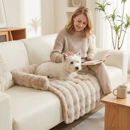 Protection-canape-chien-lit-antiderapant avec traversin entourant sur 3 côté, en fausse fourrure rembourrage 100% coton haute densité, polyvalent pour le sol, canapé, protège lit, portège siège voiture, tapis de cage, pliable, léger et portable pour petit à chien moyenne taille-dimensions 75x75 cm-un chien moyen confortablement couché sur le protège canapé pour chien en fausse fourrure douce de couleur marron clair avec traversin, caresser par sa maitresse assise sur le canapé à côté de lui qui lit un livre