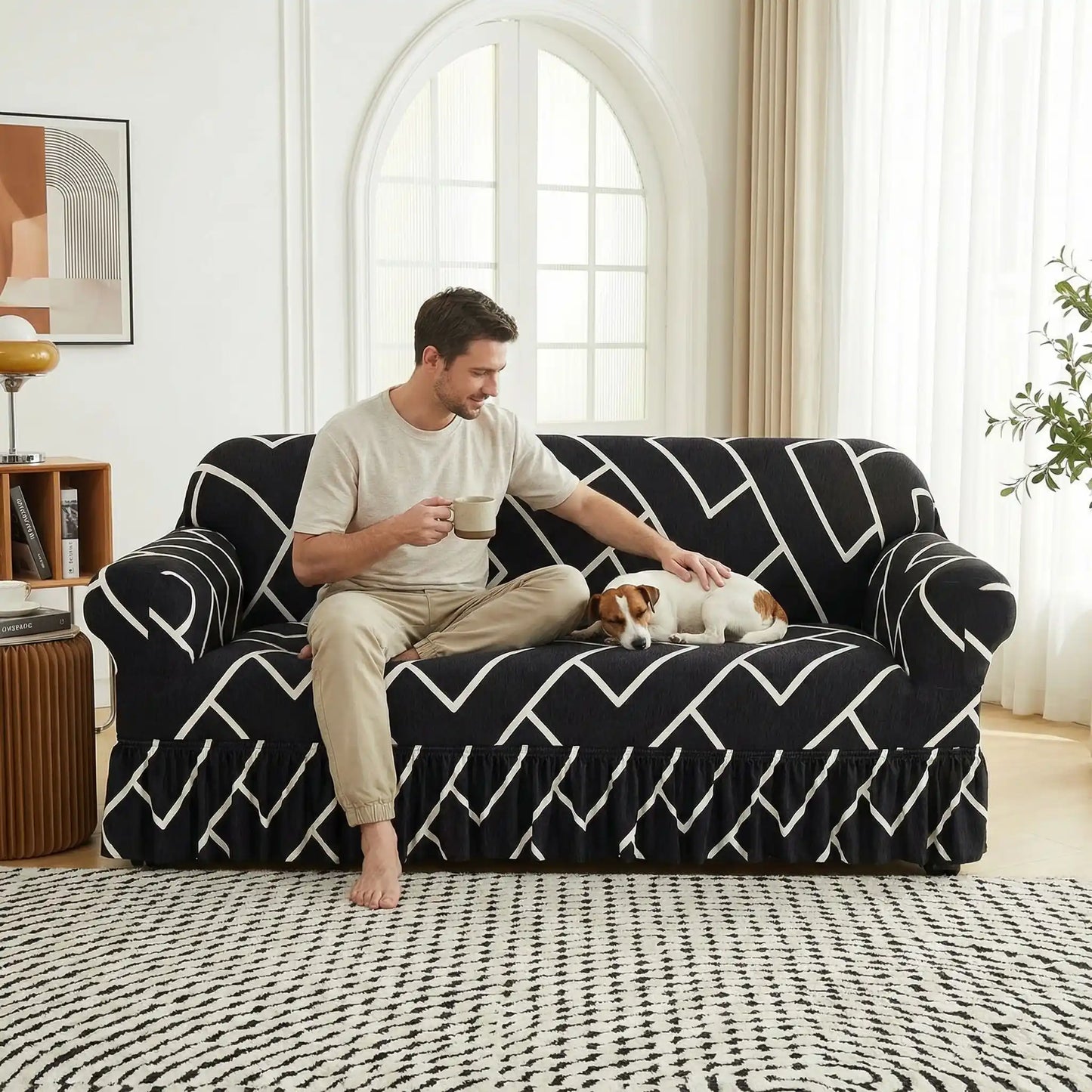 Protection-canape-chien-anti-poils-anti accident, lavable en machine, haute élasticité et resistante aux griffes et à l'usure, universelle en 4 tailles pour fauteuil, canapé de 2/3/4 places, avec élastique et bloque plis- design floral délicat- un jack russell qui dort en boule à côté de son maitre qui le caresse en buvant son café assis confortablement sur le canapé avec sa housse extensible universelle noir avec graphisme blanc dans le salon de l'appartement