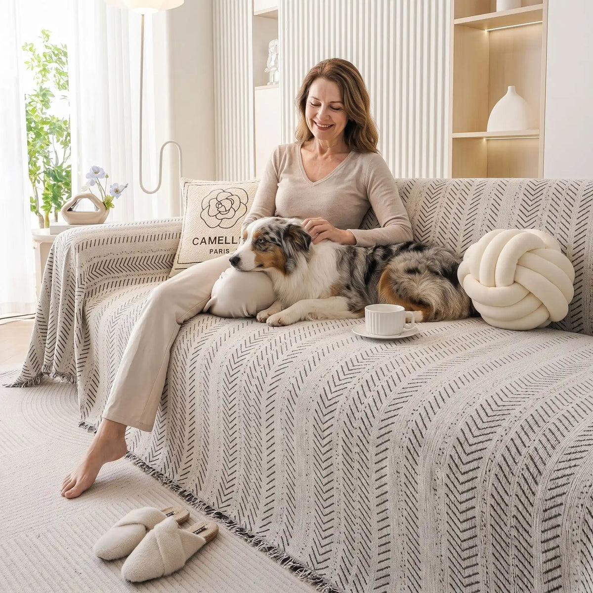 Protège-canapé-pour-chien-plaid-anti-poils-résistante aux griffes, tissage chenille coton et polyester, écoresponsable avec franges pour un style bohème chic de couleur blanc et noir disponible en 4 tailles pour fauteuil/canapé une place, deux places, 3 places et 4 places, lavable en machine, doux respirant confortable et 4 saisons-un chien de grande race couché qui se fait carresser tendrement par sa maitresse tout deux installé confortablement sur le plaid de protection du canapé du salon