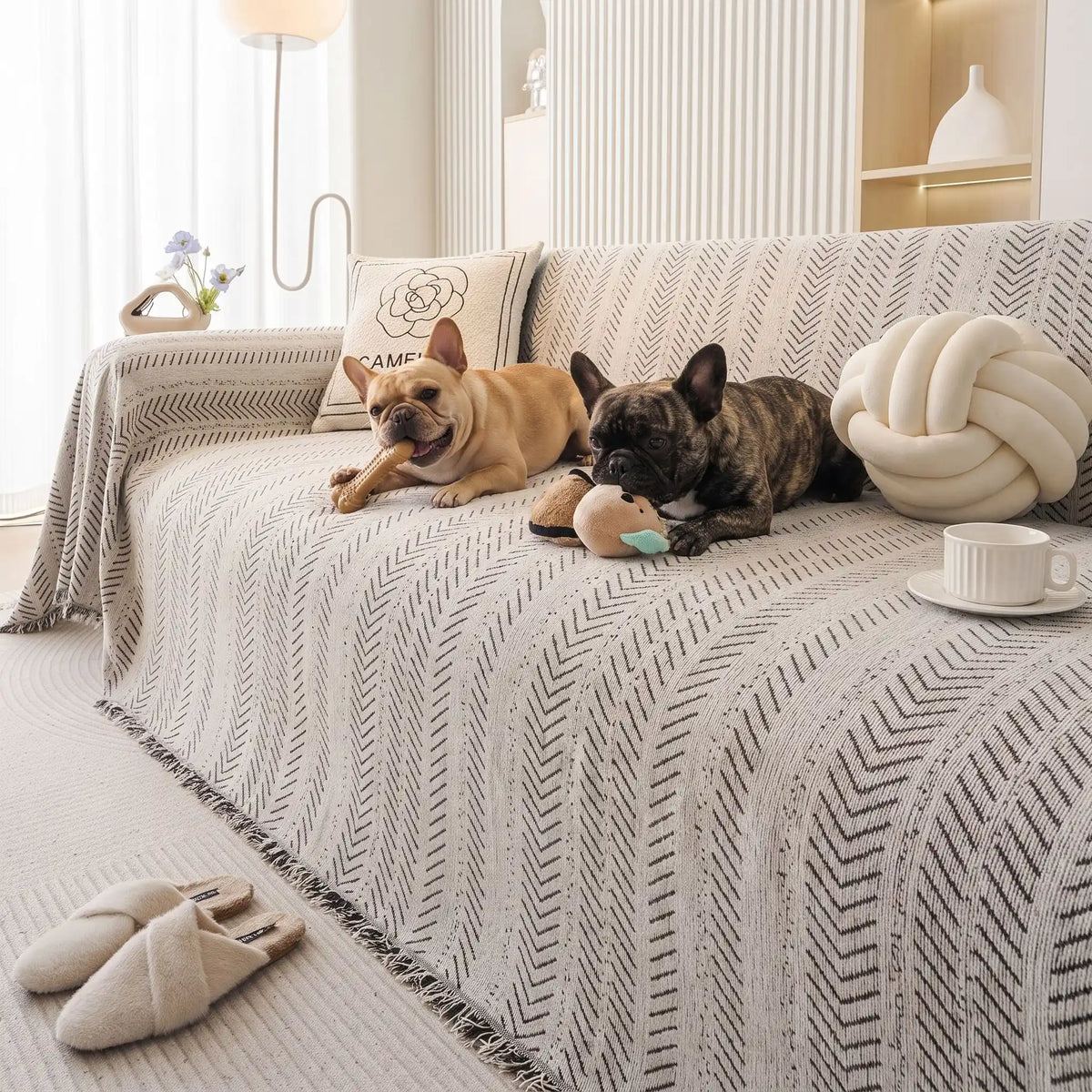 Protège-canapé-pour-chien-plaid-anti-poils-résistante aux griffes, tissage chenille coton et polyester, écoresponsable avec franges pour un style bohème chic de couleur blanc et noir disponible en 4 tailles pour fauteuil/canapé une place, deux places, 3 places et 4 places, lavable en machine, doux respirant confortable et 4 saisons-deux chiens de races moyenne qui mâchent leur jouet de mastication en toute sécurité sur le plaid au design noir et blanc souple sur le canapé du salon de la maison