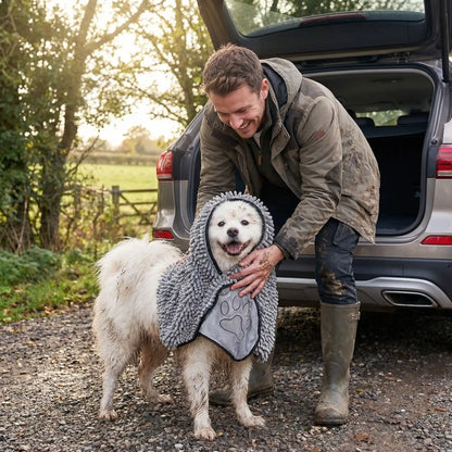 Serviette-pour-chien-microfibre-avec-chenille-douce solide et ultra-douce, lavable en machine à laver pour un séchage en profondeur, idéal après les balades, voyages, bain, toilettage avec deux poches protégés pour les mains de l'humain pour facilité le séchage sans se salir les mains-un maitre qui essuie son chien tout mouillé et plein de boue avec la serviette ultra absorbante de couleur grise avant de monter dans la voiture pour pas la salir après la balade